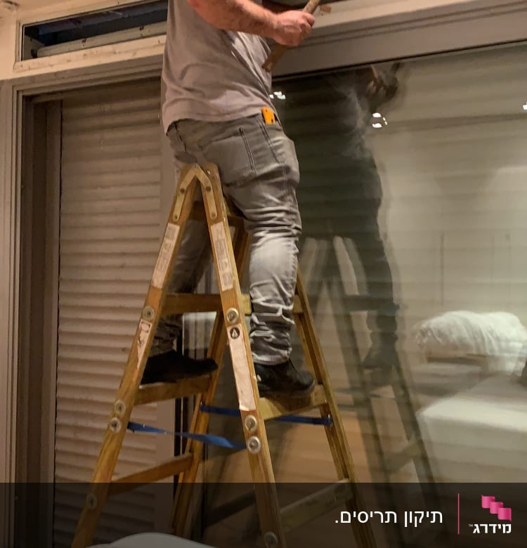 אדם על סולם מתקין תריסים עם פטיש